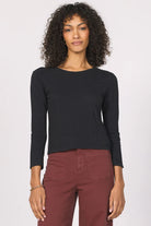 Woman wearing a black long-sleeve top and maroon pants on a white background